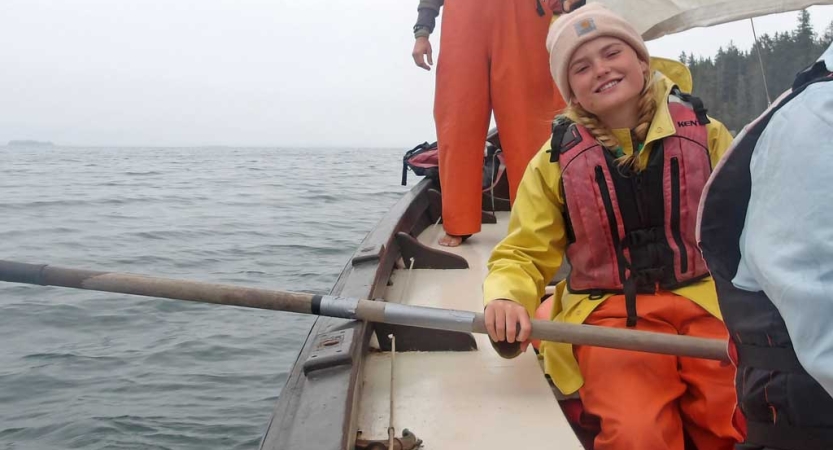 A student wearing a life jacket holds the oar of a sailboat. 